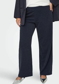 Mornarsko široke hlače iz teksturiranega blaga z kovinskimi nitmi. Kombinirane s srebrnimi čevlji s koničastim nosom in temnim jopičem.