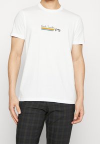 Bílá bavlněná tričko s krátkými rukávy, s barevným logem "Paul Smith" a textem "PS" na hrudi. Texturovaná látka, volný střih.