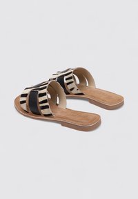 Sandalias planas con parte superior de tela a rayas en blanco y negro, con dos correas abiertas y una plantilla de cuero marrón claro con una suela marrón.