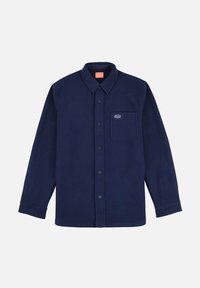 Chemise en polaire bleu marine avec une fermeture à boutons sur le devant et des manches longues. Présente une poche sur la poitrine gauche et un petit logo au-dessus. Texture douce.