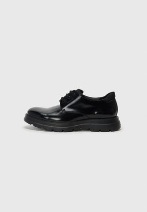 Chaussure noire en cuir à lacets avec finition lisse, semelle en caoutchouc durable et bout arrondi. Présente des œillets pour les lacets et un branding subtil.