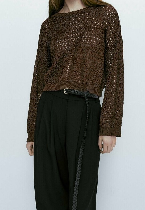 Femme portant un pull à manches longues en tricot ouvert marron, rentré dans un pantalon noir taille haute avec une longue ceinture tressée noire.