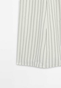 Tissu blanc avec de fines rayures verticales noires et une couture centrale avant visible en bas d'un vêtement, possiblement un pantalon ou une jupe.