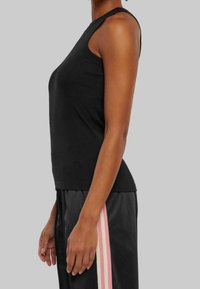 Černý tílko bez rukávů v přiléhavém střihu, vyrobené z hladké látky; doplněné o volné černé kalhoty s růžovými pruhy na bocích.