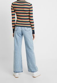 Raitainen pitkähiha-paita monivärisillä raidoilla. Väljälahkeiset vaaleansiniset farkut, joissa on rispaantunut helma. Valkoiset lenkkarit, joissa on kuvioitu pohja.