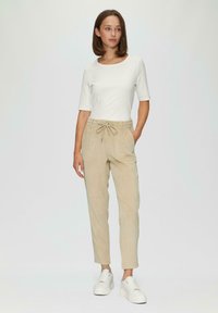 Beige corduroy broek met zijzakken en een trekkoord in de taille, gecombineerd met een witte ribbel top met korte mouwen en witte sneakers.