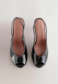 Czarne lakierowane buty typu slingback z otwartymi palcami i brązowymi wkładkami oznaczonymi "NEXT", wyeksponowane na neutralnym tle.