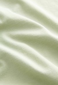 Svetlozelená bavlnená tkanina s hladkou textúrou, zobrazuje jemné záhyby a ryhy. Mäkko, flexibilne a ľahký materiál.