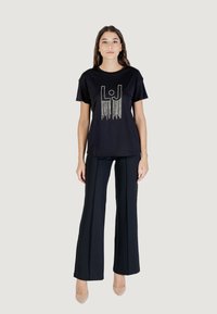 Camiseta de algodón negra de manga corta con un diseño gráfico con flecos de color claro en la parte delantera, combinada con pantalones negros ajustados.
