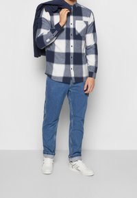 Camisa de manga larga de cuadros en azul marino y blanco con un bolsillo en el pecho, combinada con jeans de mezclilla azul y zapatillas blancas. Diseño minimalista.