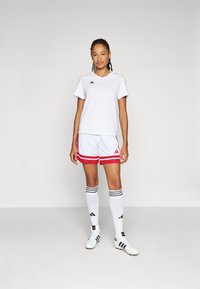 Witte sportt-shirt, korte broek met rode accenten, zwart logo, gestreepte sokken, witte voetbalschoenen. Eenvoudig ontwerp, lichtgewicht stof, sportieve pasvorm.