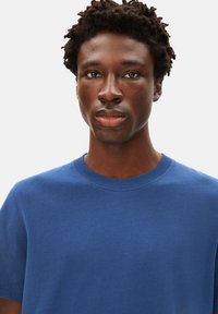 T-shirt bleu en coton à col rond, avec des manches courtes et une texture lisse, présenté sur un fond clair.