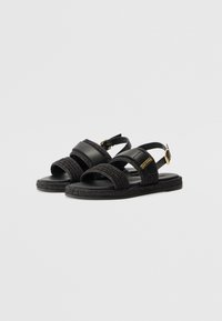 Sorte sandaler med vævede tekstilremme, en glat lædersål og en lille hardwaredetalje i guldfarve på ankelremmen.