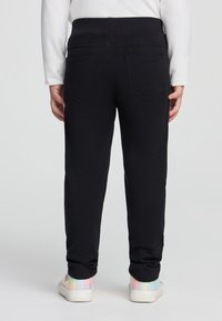 Pantaloni della tuta neri con una texture liscia, dotati di due tasche posteriori e polsini elasticizzati. Abbinati a sneakers color pastello arcobaleno.