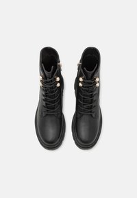 Botas de cuero negro hasta el tobillo con punta redonda, parte delantera con cordones, herrajes en tono dorado y acentos decorativos de perlas en los cordones.