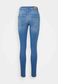 Jeans skinny de denim azul claro, com cintura média, dois bolsos traseiros e bainhas desfiadas nos tornozelos.