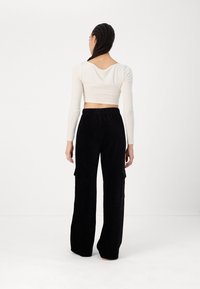 Witte lange mouwen crop top met een ronde rug; zwarte wijde corduroy broek met cargo zakken, zachte textuur, elastische tailleband.