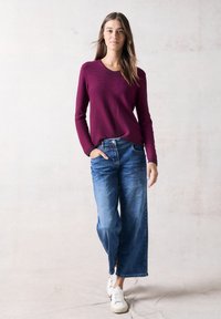 Bordeaux langemouwen trui gecombineerd met wijdvallende blauwe jeans en witte sneakers, met een ontspannen pasvorm en een basic ronde halslijn.