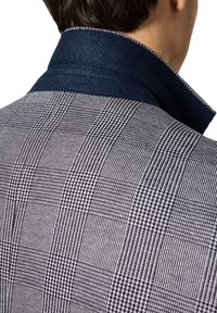 Szary i czarny wzorzysty żakiet o teksturowanym wzorze w jodełkę, z ciemnoniebieskim filcowym kołnierzem i kontrastującymi detalami w szwie.