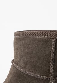 Acercamiento a la parte superior de una bota de ante marrón con costuras visibles y un ribete de tela a lo largo del borde superior.