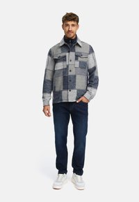 Rutete skjortejakke i grått og marineblått, med fire frontlommer, krage og knappeåpning, kombinert med mørke jeans og sneakers.