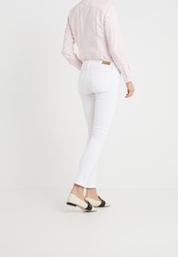 Jeans skinny bianchi in materiale cotone, con tasche posteriori e cuciture a contrasto, abbinati a scarpe slip-on beige e nere, creando un look sartoriale.