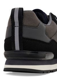Men's athletic shoe featuring a gray woven upper with black suede accents, a flat rubber sole, and a distinct black and gray pull tab.