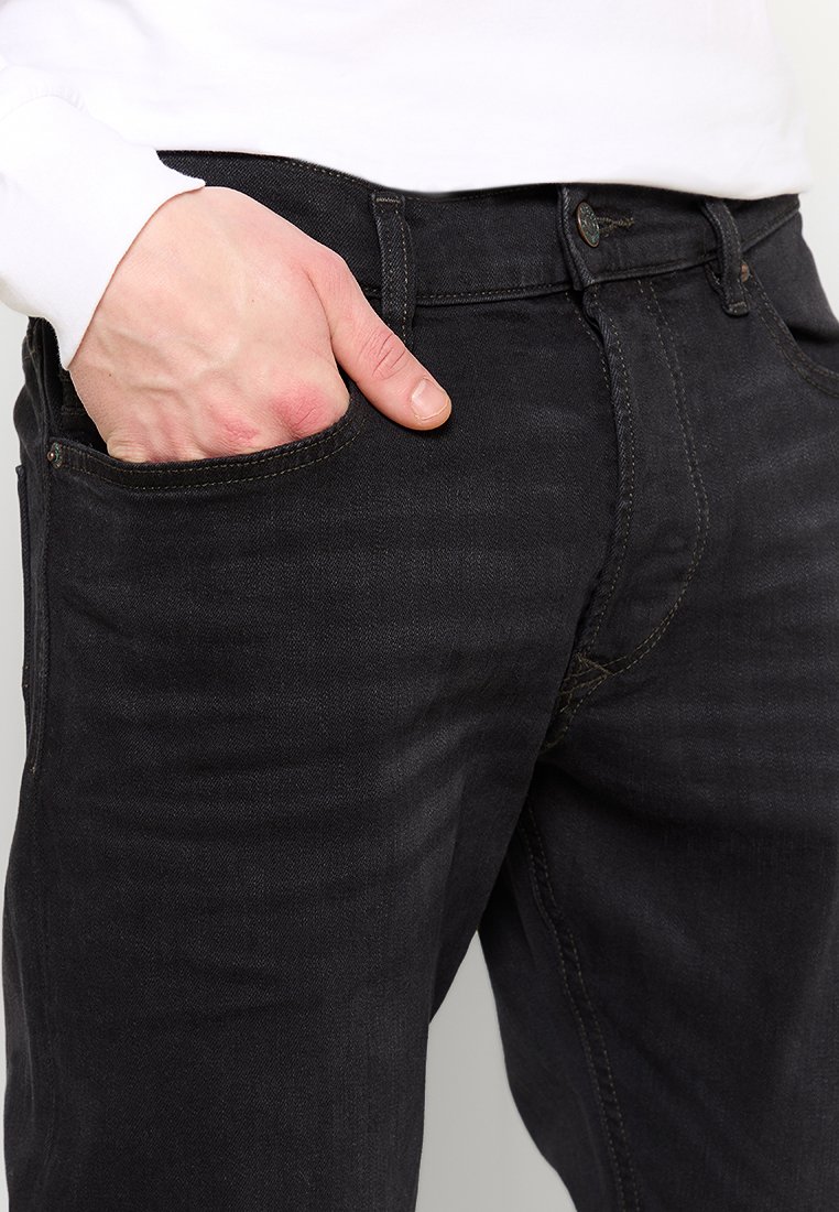 Jeans en denim noir à coupe ajustée, avec une poche avant et des détails de couture subtils. La taille est dotée d'une fermeture à un seul bouton.