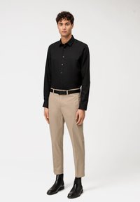 Maglietta nera a maniche lunghe; pantaloni beige; cintura nera; stivali neri alla caviglia; tessuto liscio; taglio slim; design con bottoni; stile minimalista.