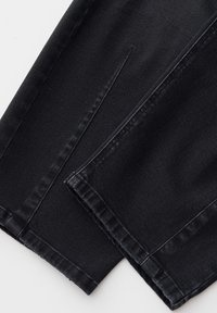 Close-up of black denim fabric showing stitched hems and seams on overlapping pant legs.