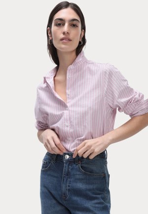 Hellrosa und weiß gestreifte Button-Up-Bluse mit Stehkragen, hochgerollten Ärmeln und weicher Textur, kombiniert mit hochgeschnittenen blauen Jeans.