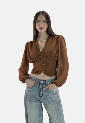 Blouse marron ajustée avec un décolleté en V profond et des manches bouffantes, comportant 7 petits boutons sur le devant ; associée à un jean bleu clair ample.