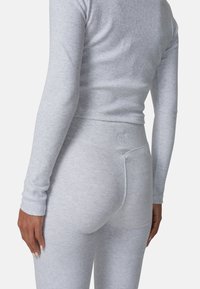 Jasnoszary, prążkowany top z długim rękawem i dopasowane legginsy z wysokim stanem. Miękka tekstura z subtelnym wzorem i wytłoczonym logiem na pasie.