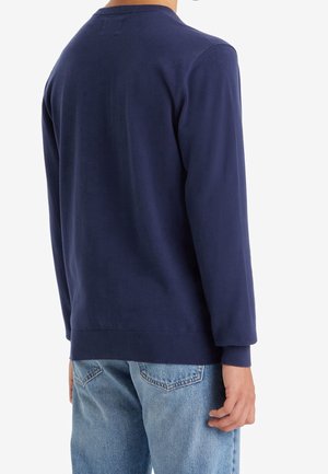 Navy blue sweatshirt with long sleeves, round neckline, and ribbed cuff. Worn with light blue denim jeans, displaying a relaxed fit.