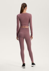 Fitted long-sleeve top and leggings in muted mauve fabric, showcasing ribbed texture and a cropped design, paired with black athletic shoes.