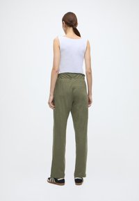 Πράσινο, άνετο παντελόνι με κορδόνι στη μέση, σε συνδυασμό με λευκό αμάνικο τοπ. Το στυλ είναι καθημερινό και άνετο.