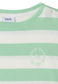 Chemise à rayures vertes et blanches avec encolure ronde, étiquette « CECIL » et texte circulaire « Sois gentil avec ton esprit » sur la poitrine.