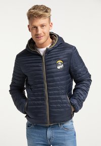 Giubbotto imbottito navy con design trapuntato, chiusura con zip e cappuccio. Presenta un patch con logo sul petto e zip e fodera a contrasto.