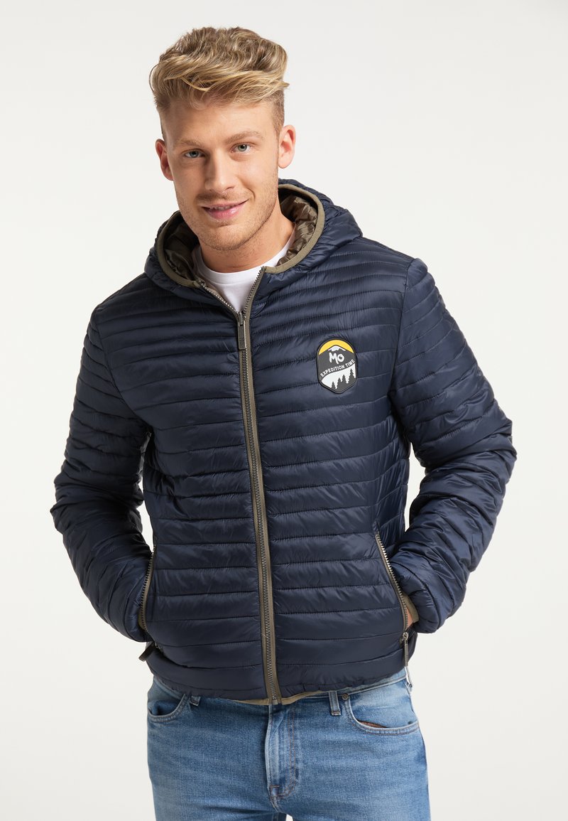 Giubbotto imbottito navy con design trapuntato, chiusura con zip e cappuccio. Presenta un patch con logo sul petto e zip e fodera a contrasto.