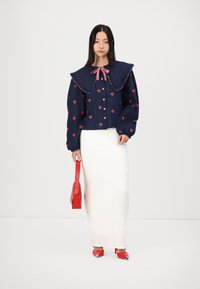 Ναυτικό μπλε σακάκι με σχέδια καρδιάς, υπερμεγέθης γιακάς και ροζ φιόγκο; λ�ευκή υφασμάτινη φούστα; κόκκινη τσάντα χειρός; κόκκινα παπούτσια με ασημί λεπτομέρειες.