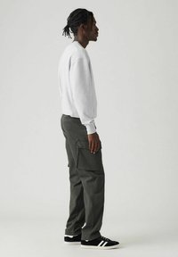 Grauer Pullover, olivfarbene Cargohosen mit Seitentaschen, schwarze Sneakers mit weißen Streifen. Glattes Material, lässiger Schnitt und entspanntes Design.