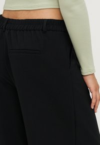 Black wide-leg trousers with an elastic waistband and a back pocket. The fabric appears soft and slightly textured.