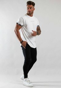 Vitt kortärmat t-shirt med mönstrade svarta mudd, parat med åtsittande svarta byxor och vita sneakers. Modern, atletisk design.