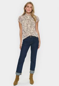 Cream floral blouse with ruffled front, short sleeves, and high neck; paired with dark blue jeans and tan ankle boots.