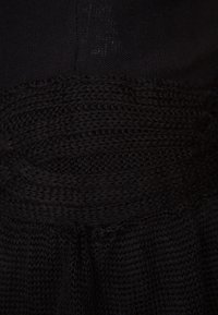 Schwarzes Strickkleid mit einer strukturierten Optik, geripptem Detail am Taillenbereich und glattem Stoff darunter.