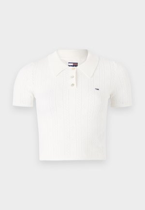 Fehér trikó, rövid ujjakkal, bordázott gallérral, három gombbal, függőleges textúra mintákkal, és egy kis márkás logóval a bal oldalon.