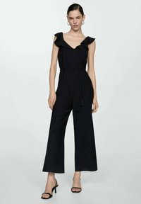 Svart jumpsuit med volangärmar, V-ringning och flätad bälte med tofsar. Vidbenad design, tillverkad av ett lättviktigt material.