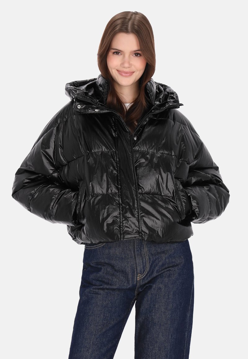 Fekete, fényes hatású pufidzseki cipzáras elülső résszel, levehető kapucnival és oldalzsebekkel. Fehér felső és kék farmer felett viselve.