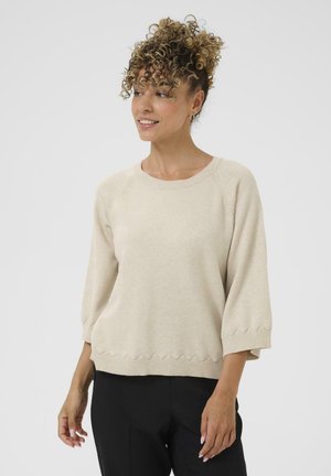 Pull en maille beige avec un col rond et des manches trois-quarts. Des détails en bordure festonnée et une texture accentuent le design.