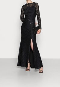Černé krajkové večerní šaty s dlouhými rukávy, se zdobením z flitrů, přiléhavý střih a rozparek ke stehnu. Doplněné kabelkou a lodičkami.